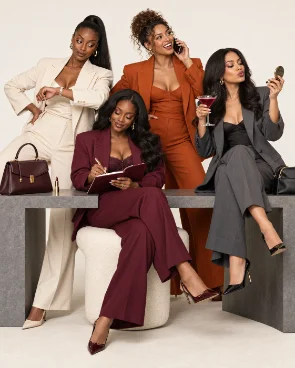 Four women in tailored suits sitting together, one writing in a notebook