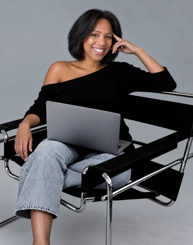 Marika Bee smiling in a chair with a laptop on her lap